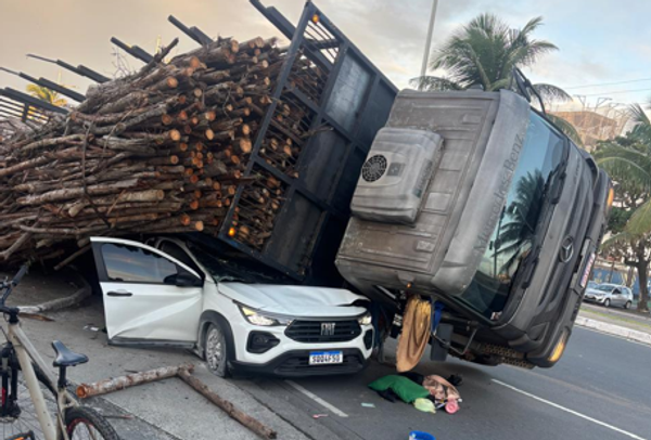 caminhão que transportava madeira tombou sobre um carro de passeio na tarde desta quarta (1º), em Pituaçu.| Reprodução/ Redes Sociais